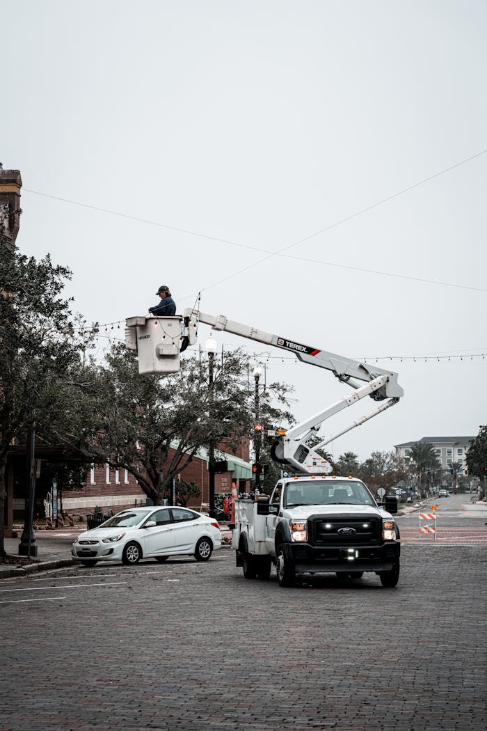services-04 Urban streetscape with city workers fixing streetlights using a cherry picker truck on an overcast day.