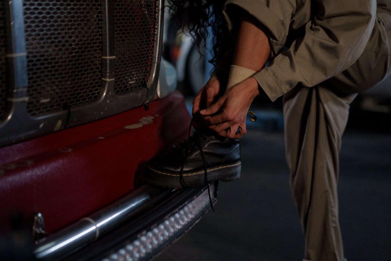 services-02 Close-up of a woman in work attire tying her boot on a truck bumper, emphasizing resilience.